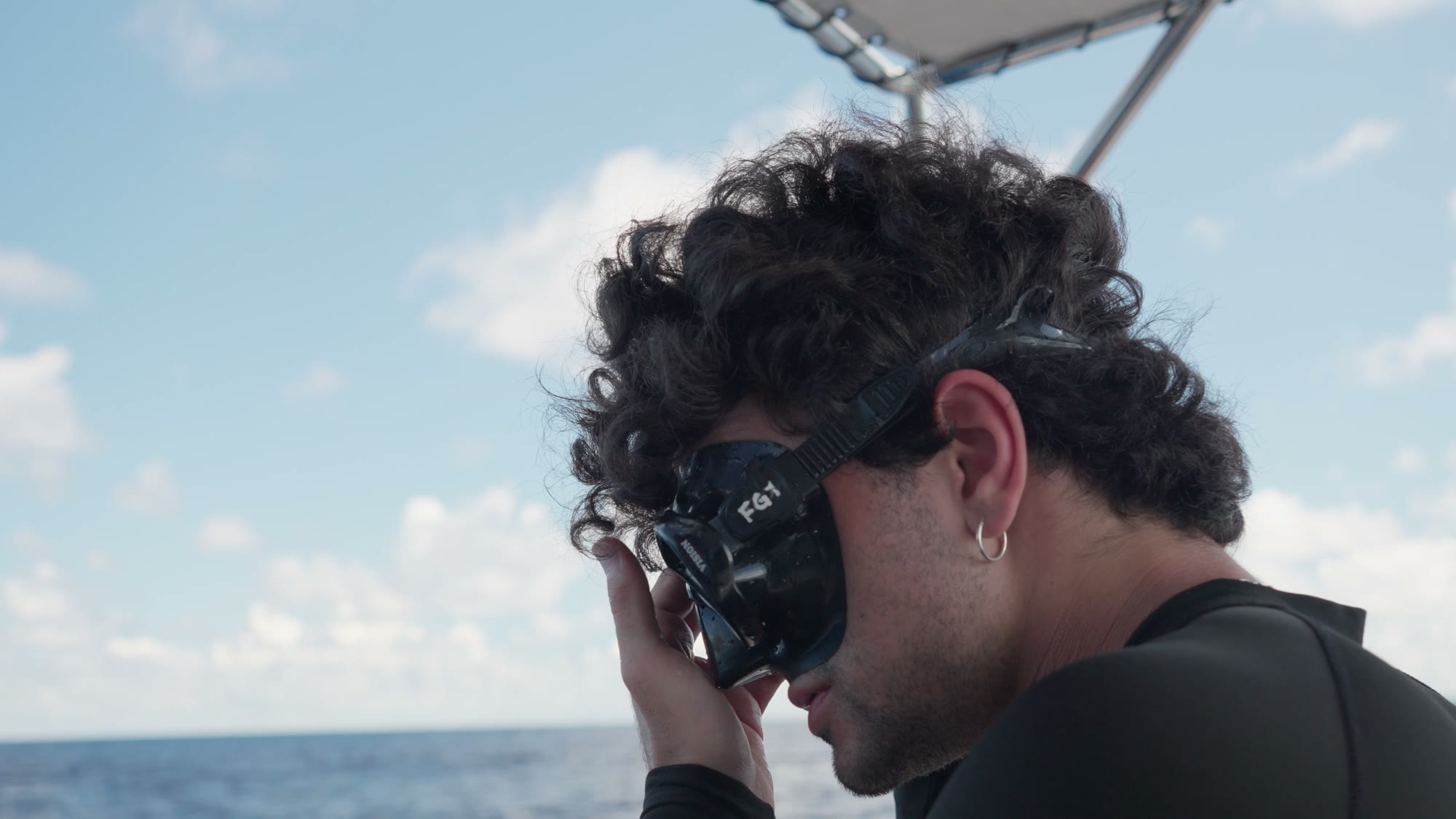 The 2026 winner pulling on a dive mask on the boat.