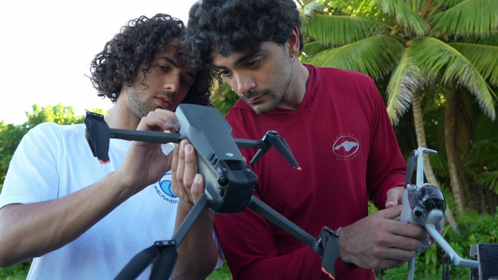 The 2026 winner and a fellow traveller setting up a drone under the palms.